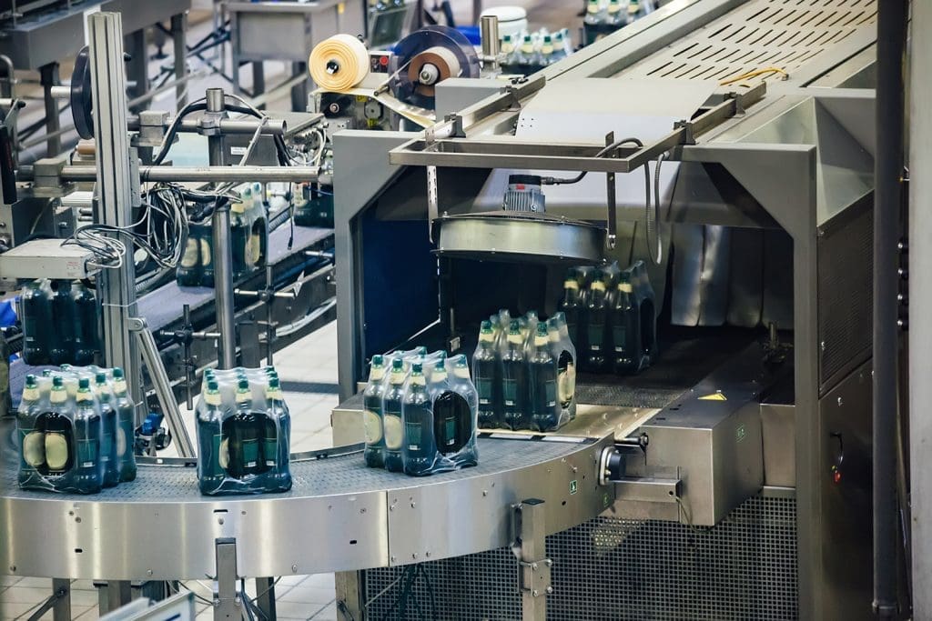 Shrink-wrapped bottles moving down a conveyor and into a packaging machine