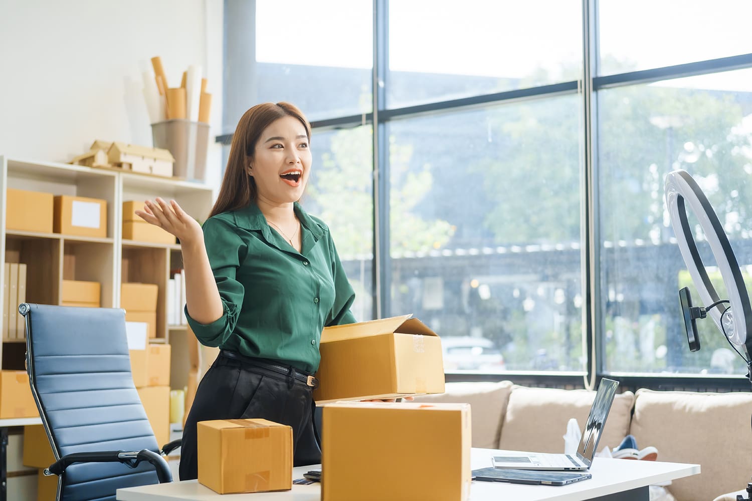 A woman in an office room holds and stands among brown packaged boxes