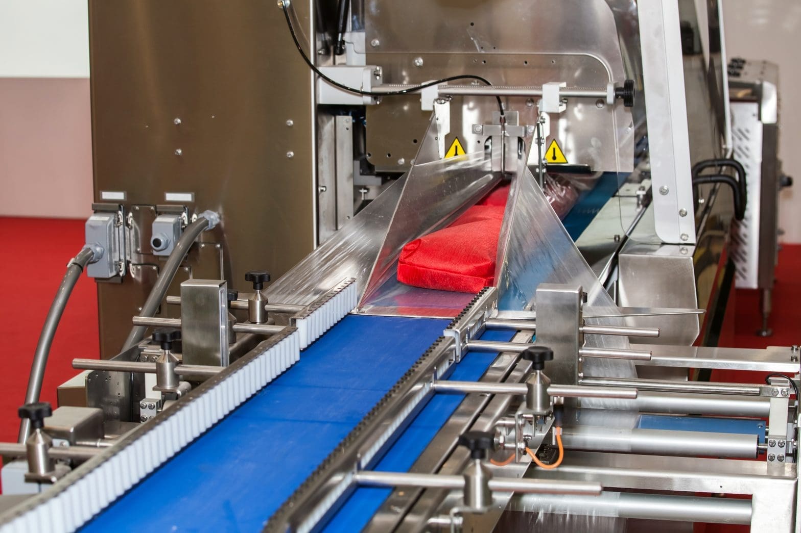 a red product going through a packaging process where it is wrapped in a plastic film by a machine