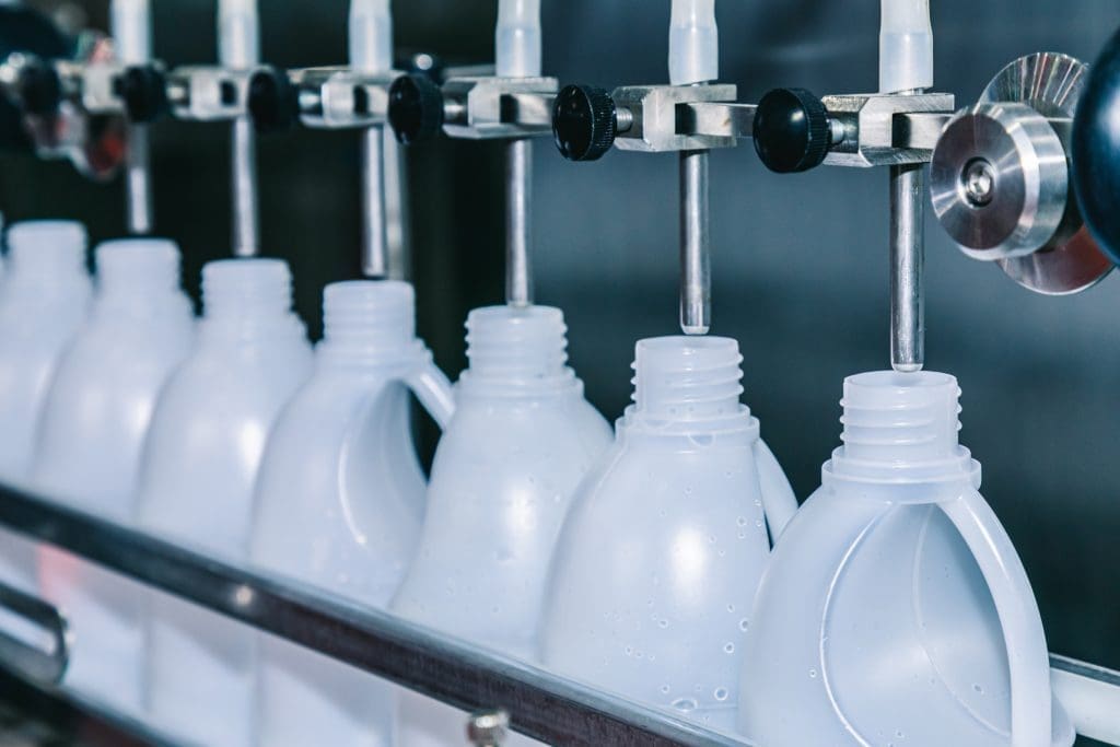 White plastic bottles with handles being filled on a production line