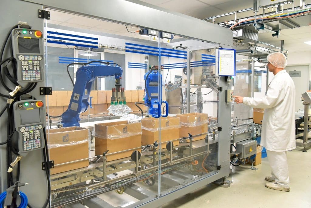 A person works with a robotic packaging line, pressing a button as the blue robotic arms work.