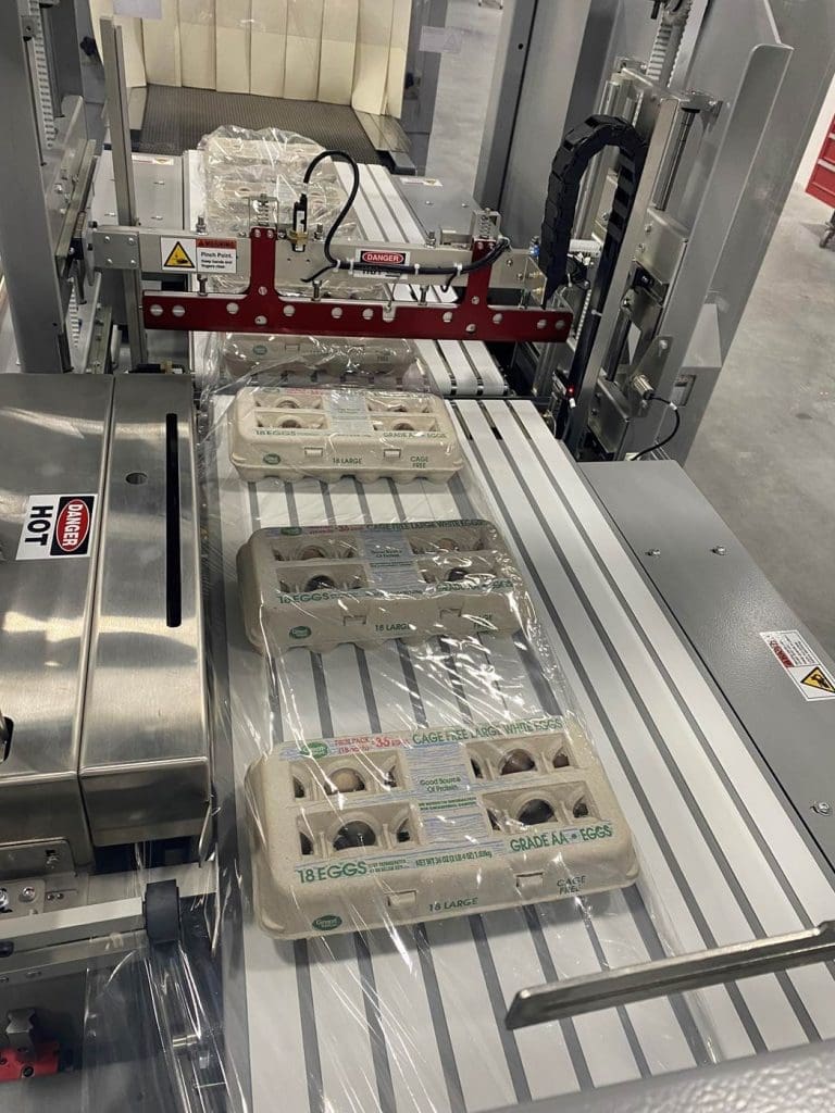 18-count cartons of eggs on a conveyor belt of a shrink wrap machine